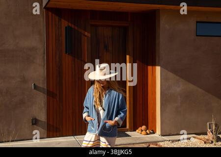 Frau draußen in der Wüste mit Hut vor einem modernen Zuhause Stockfoto