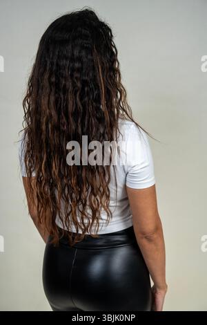 Studio-Aufnahme einer jungen Frau mit langen lockigen Haaren, von hinten gesehen, mit weißem T-Shirt und schwarzer Leggings Stockfoto
