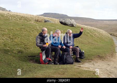 Drei (Männer) Wanderer sitzen/sprechen auf der Bank in der Nähe von Crina Bottom auf der Route Ingleborough, einem der Yorkshire 3 Peaks von Ingleton in den Yorkshire Dales. Stockfoto