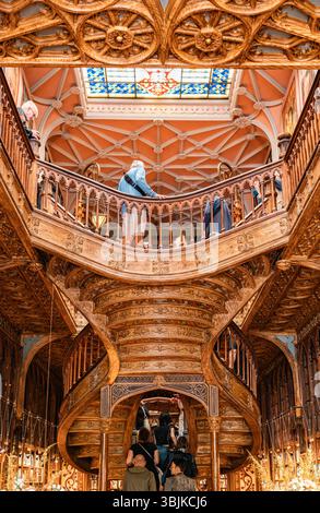 Besucher bewundern die komplizierte Holztreppe und die Buntglasdecke im berühmten Buchladen Livraria Lello, ein kulturelles Wahrzeichen und architektonisches Juwel. Porto, Portugal - 11. Juni 2025 Stockfoto