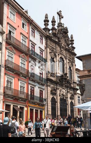 Touristen spazieren vorbei an der prunkvollen barocken Igreja dos Clerigos und pulsierenden historischen Gebäuden in einer lebhaften Straßenszene von Porto. Porto, Portugal - 11. Juni 2025 Stockfoto