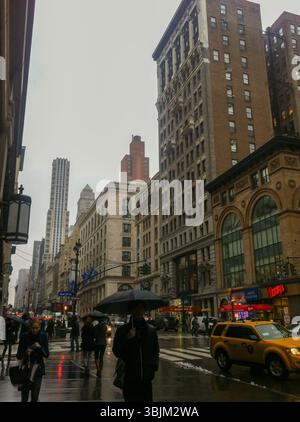 NEW YORK, USA – 19. MÄRZ 2013: Menschen mit Sonnenschirmen laufen bei Regen entlang der Fifth Avenue. Gelbe Taxis und Ladenfronten sind zu sehen. Stockfoto