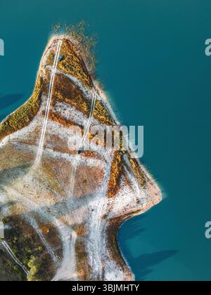 Atemberaubendes Drohnenfoto einer dreieckigen Halbinsel mit sich kreuzenden unbefestigten Straßen, lebendiger Vegetation und klarem blauem Wasser, aufgenommen in den malerischen Landschaften Südspaniens. Stockfoto