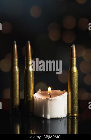Ein konzeptionelles Stillleben mit einer beleuchteten Kerze und einer Gewehrkugel in unmittelbarer Nähe, fotografiert in dezenter Beleuchtung. Stockfoto