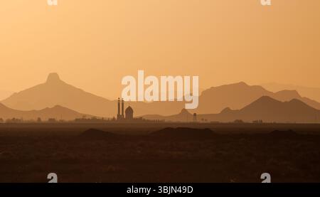 Silhouette einer Moschee bei Sonnenuntergang in Zentral-Iran, mit mehrschichtigen Hügeln, die unter warmem Licht in einer ruhigen Wüstenlandschaft in die Ferne fallen. Stockfoto