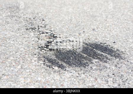 Ein schwarzer Asphaltwischer, der auf einer rauen Betonoberfläche sichtbar ist und urbane Elemente und Details zeigt Stockfoto