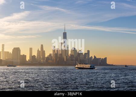 Fähre überquert den Hudson River bei Sonnenaufgang mit Blick auf das Finanzviertel, einschließlich One World Trade Center. Stockfoto