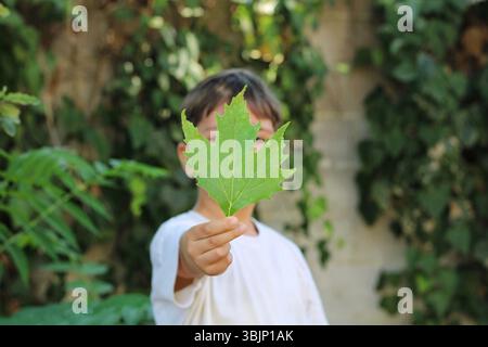 Kind, das draußen ein grünes Blatt vor dem Gesicht hält, symbolisiert Umweltbildung, Beobachtung und frühe Naturforschung. Stockfoto