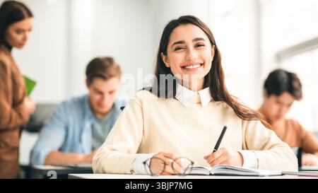 Lächelnde Schülerin, die am Schreibtisch sitzt und in ihr Notizbuch schreibt Stockfoto