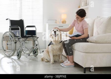 Mädchen mit Behinderung, das Buch liest, und ihr Diensthund zu Hause Stockfoto