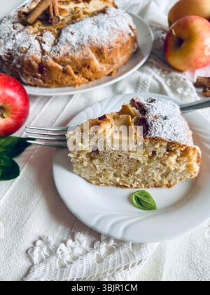Ein Stück köstlicher hausgemachter Apfelkuchen, dekoriert mit Zimtstangen und frischen Äpfeln im Hintergrund. Direkt darüber. Stockfoto
