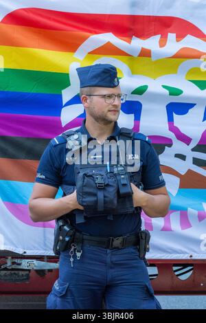 Polizeibeamter steht vor einer Regenbogenfahne bei der Warschauer Pride Parade; Warschau, Woiwodschaft Masowien, Polen; Juni 2025 Stockfoto
