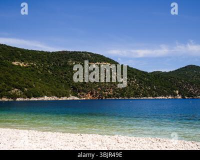 Die Küstenklippen und das pulsierende Wasser des Antisamos Strandes auf Kefalonia glänzen unter der Sonne und dem wolkenlosen mediterranen Himmel. Stockfoto
