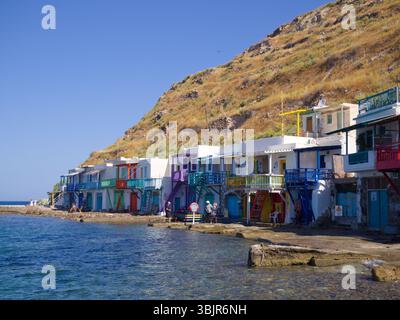 Milos, Griechenland – Einheimische und Besucher genießen einen sonnigen Nachmittag am Meer im Dorf Klima. Die Szene zeigt farbenfrohe Häuser am Meer und ruhiges Wasser. Stockfoto