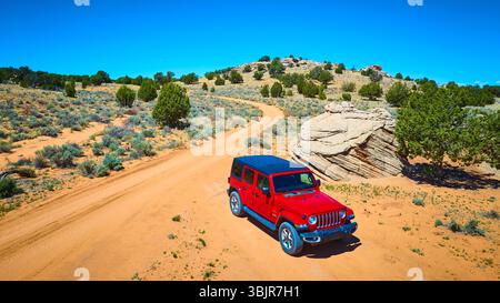 Roter SUV auf der gewundenen Desert Road mit Felsformationen und Wacholderbäumen Stockfoto