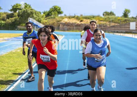 Entschlossene junge Athleten, die auf einer blauen Strecke laufen und bei einem Leichtathletikwettbewerb den Sieg anstreben Stockfoto