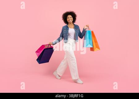 Glückliche junge schwarze Frau, die selbstbewusst mit bunten Einkaufstaschen geht Stockfoto