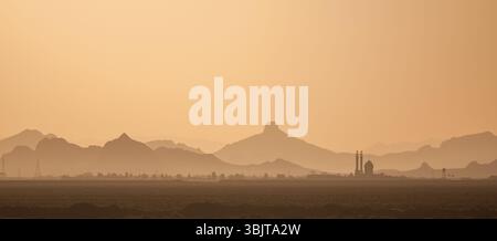 Silhouette einer Moschee bei Sonnenuntergang in Zentral-Iran, mit mehrschichtigen Hügeln, die unter warmem Licht in einer ruhigen Wüstenlandschaft in die Ferne fallen. Stockfoto