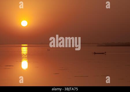 Traditionelles Kanu auf dem Fluss Niger bei Sonnenuntergang in der Nähe von Ségou, Mali, mit einem orange leuchtenden Himmel über ruhigem Wasser in einer ruhigen westafrikanischen Szene. Stockfoto