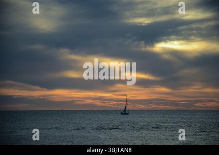 Sonnenuntergang über der Bucht von Punta del Este mit Silhouette eines einsamen Segelboots. Stockfoto