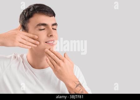 Junger Mann, der Gesichtsbauübung auf hellem Hintergrund macht Stockfoto