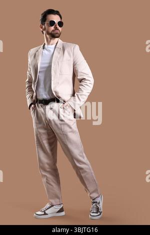 Hübscher junger Mann in hellem Anzug mit Sonnenbrille auf beigem Hintergrund Stockfoto