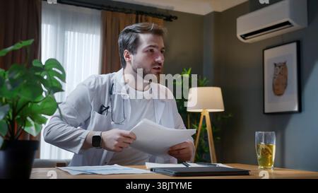 Ein Arzt mit Brille und Stethoskop überprüft Patientendokumente in einer modernen Praxis. Mit einem fokussierten Ausdruck analysiert er medizinische Aufzeichnungen Stockfoto