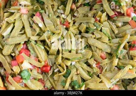 Es wird ein lebhafter Kaktussalat mit fein geschnittenen Kaktusscheiben, frischen Tomaten, Zwiebeln und Koriander zubereitet. Gehackte Chilischoten Stockfoto