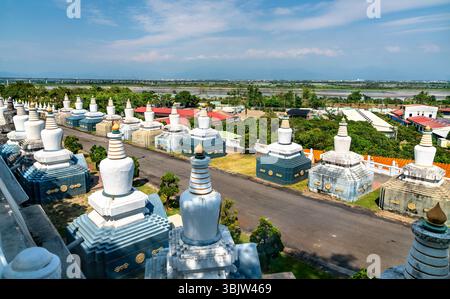 Reihen weißer Stupas säumen einen ruhigen Pfad im Fo Guang Shan Kloster in Kaohsiung, Taiwan, mit einer traditionellen chinesischen Pagode, die unter einem klaren blauen Himmel durch die Bäume sichtbar ist Stockfoto