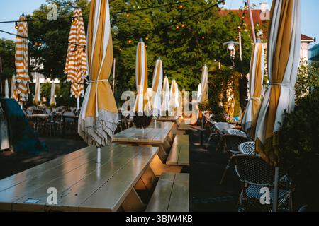 Gefaltete und geschlossene große Sonnenschirme, Tische und Stühle im Straßenrestaurant oder Café in Europa. Sonniger Sommermorgen vor der Öffnungszeit, keine Leute Stockfoto