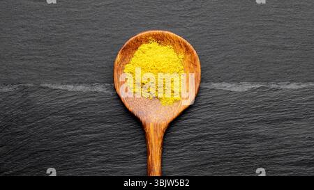 Bunte Gewürze auf Holzlöffeln – Curry, Kurkuma und Paprika auf dunklem Schiefergrund Stockfoto