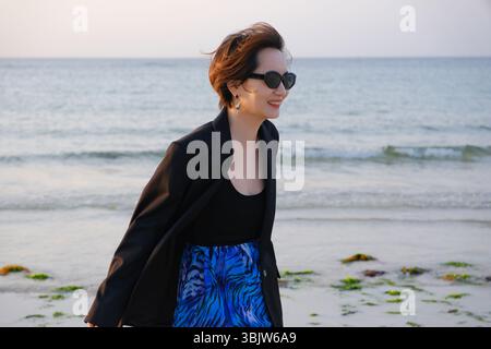 Lächelnde Kurzhaarasiatische Frau in Sonnenbrille mit Meerblick. Reisen Sie in Jeju, Südkorea Stockfoto