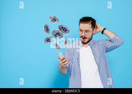 Kryptowährung. Überraschter Mann mit Smartphone auf hellblauem Hintergrund. Bitcoins fliegen aus dem Gerät Stockfoto