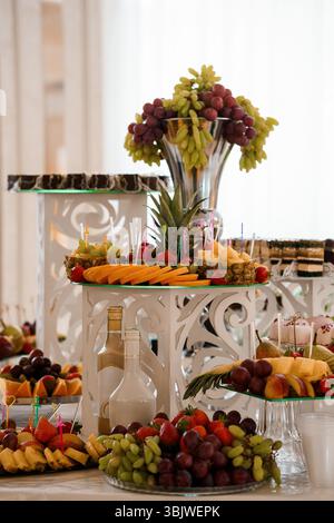 Ein üppig gestaltetes Obstbuffet bietet eine lebhafte Auswahl an frischen Früchten wie Trauben, Ananas, Erdbeeren und Melonen, die in kunstvoll verzierten C präsentiert werden Stockfoto