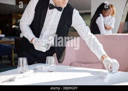 Junger Erwachsener, kaukasischer Mann, der einen Tisch in der Hand hält, während er Glas im Restaurant hält Stockfoto