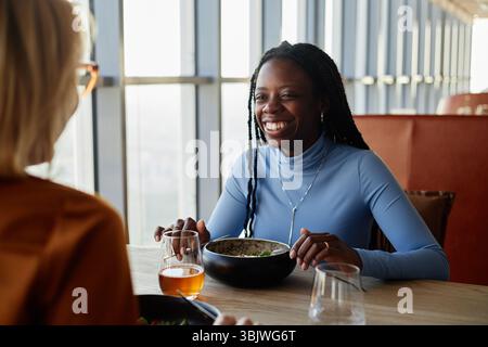 Junge Erwachsene Schwarze Frau lächelt beim Mittagessen mit einer Kaukasierin Stockfoto