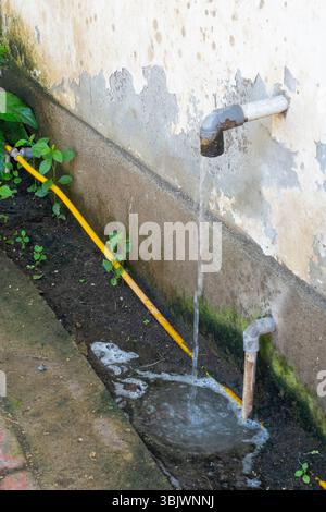 Das gelbe Rohr tropft Wasser auf den Boden. Das Wasser kommt aus einem Rohr, das an einer Wand befestigt ist Stockfoto
