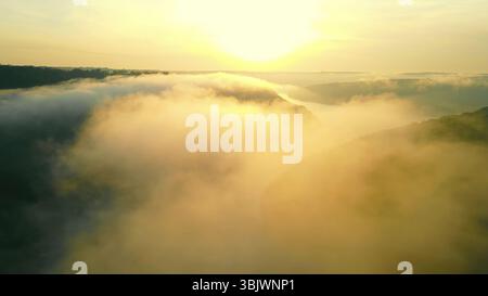 Nebliger Sonnenaufgang über einem Flusstal. Ein atemberaubender Blick aus der Luft auf einen nebeligen Sonnenaufgang über einem Flusstal, umgeben von dickem Nebel. Stockfoto