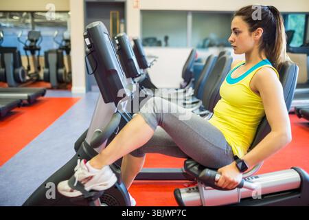 Frau, die im Fitness-Studio Liegefahrrad in die Pedale tritt, Spiegelwand reflektiert Kardio-Geräte Stockfoto
