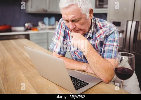 Silberner Laptop, offen auf Holztisch in moderner Küche mit einem Glas Rotwein Stockfoto