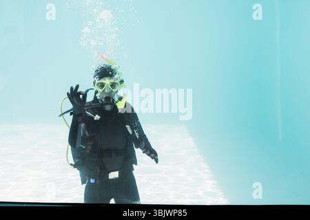 Taucher mit gelber Tauchermaske und Tauchbecken, die im klaren Poolwasser schweben, Blasen steigen auf Stockfoto