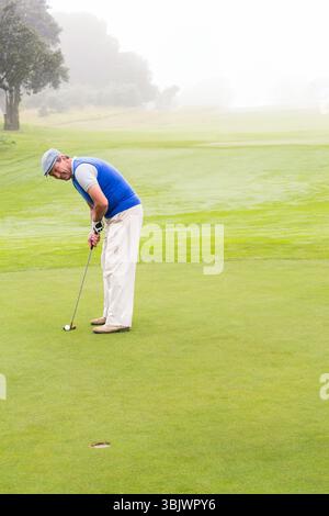 Senior Afroamerikaner mit flacher Kappe, der Putter über Golfball auf Putting Green hält Stockfoto