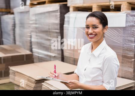 Hispanische Frau überprüft Inventar mit Klemmbrett und rotem Stift im Lagerbereich, Kopierraum Stockfoto