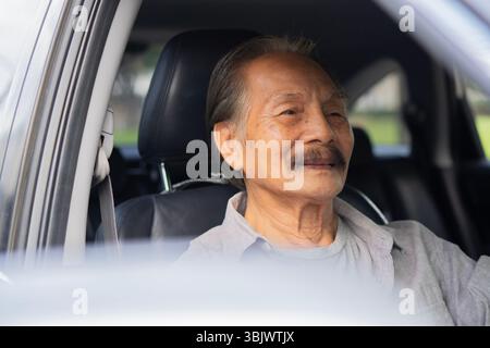 Porträt eines lächelnden asiatischen Seniors, eines alten Mannes, eines älteren Mannes, der ein Auto fährt. Das Konzept des glücklichen Alters und der Rente. Stockfoto