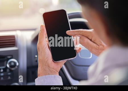 Rückansicht eines Mannes mittleren Alters, der im Auto sitzt, zeigt Smartphone mit leerem dunklen Bildschirm, mobile App für Navigation, Modell Stockfoto