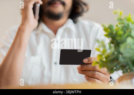 Selektiver Fokus eines erwachsenen bärtigen Mannes, der Kreditkarte hält und am Handy spricht. Bezahlung mit Kreditkarte Online-Konzept. Stockfoto