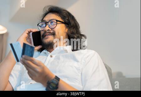 Schuss von einem glücklichen gutaussehenden bärtigen Mann, der zu Hause Handy und Kreditkarten benutzt. Kopierbereich. Online-Bezahlung mit Kreditkartenkonzept. Stockfoto
