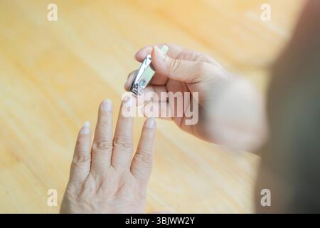 Rückansicht der alten Frauenhände mit Nagelschnitt über Holztisch. Schneidnagelkonzept. Kopierbereich. Stockfoto