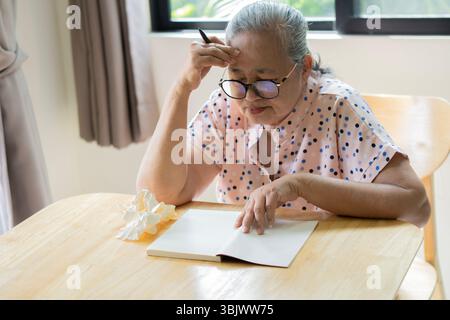 Porträt einer traurigen Seniorin, die am Holztisch sitzt und einen Brief schreibt. Schreibkonzept für ältere Menschen. Rentenprouble-Konzept. Stockfoto