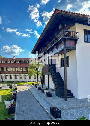 Wunderschöne traditionelle Klostergebäude auf dem Balkan mit Holzbalkonen, weißen Wänden und Blumentöpfen vor einem leuchtend blauen Himmel. Stockfoto
